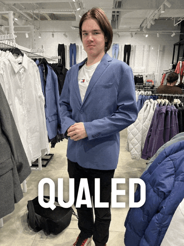 a man in a blue jacket is standing in a clothing store and the word qualed is on the bottom right