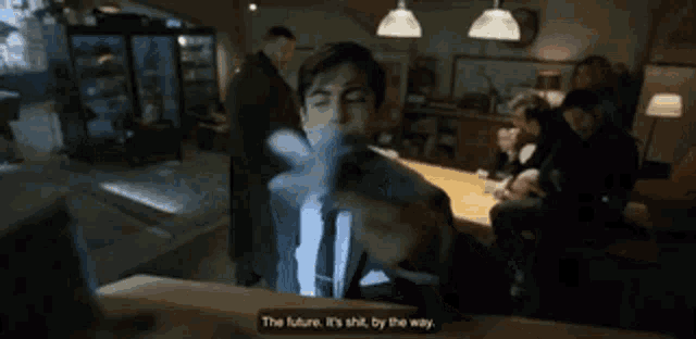 a man in a suit and tie is sitting at a table with a sign that says the future is shit by the way .