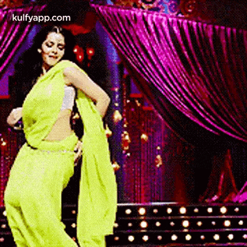 a woman in a yellow saree is dancing on stage .