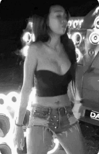 a black and white photo of a woman in a crop top and shorts dancing in front of speakers .