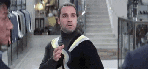 a man in a black turtleneck sweater is pointing at another man in a clothing store .