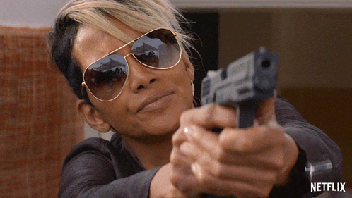 a woman wearing sunglasses is pointing a gun at the camera with the netflix logo in the corner