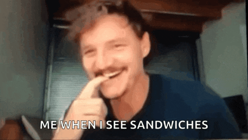 a man with a mustache is eating a sandwich with his finger in his mouth .
