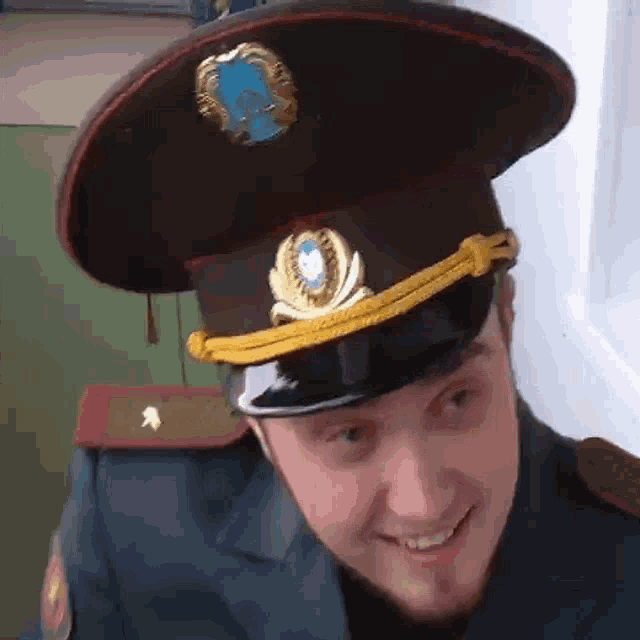 a man in a military uniform is smiling and wearing a hat with a blue emblem on it