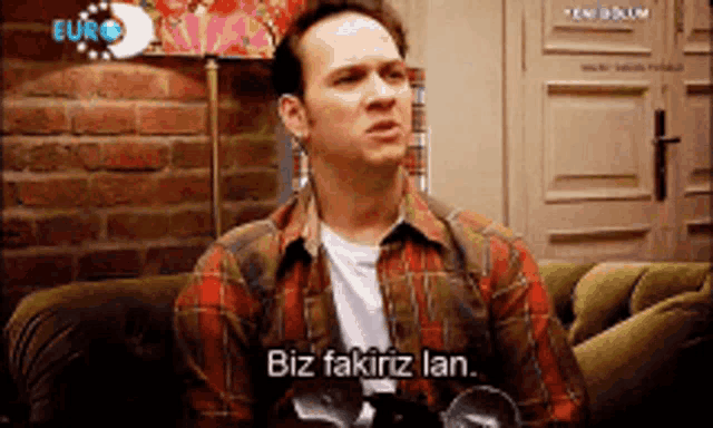 a man in a plaid shirt is sitting on a couch with the words biz fakirz lan on the screen