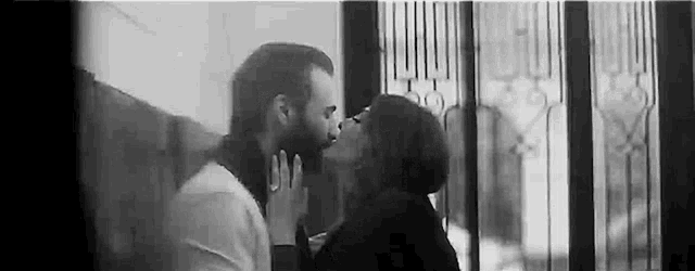 a man and a woman are kissing in front of a window .