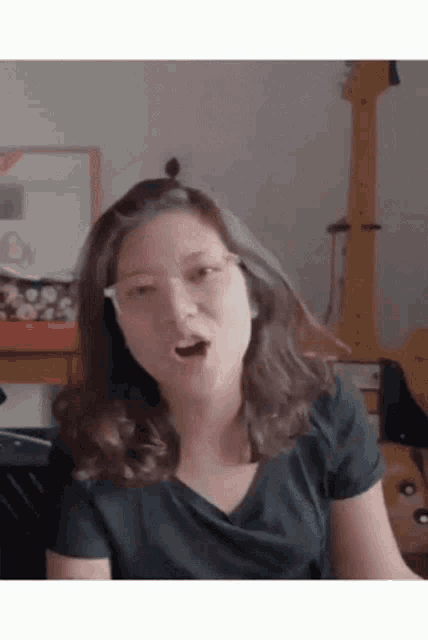 a woman wearing glasses and a black shirt is making a funny face with her mouth open .
