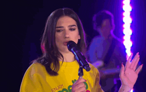 a woman singing into a microphone with the word enjoy on her shirt