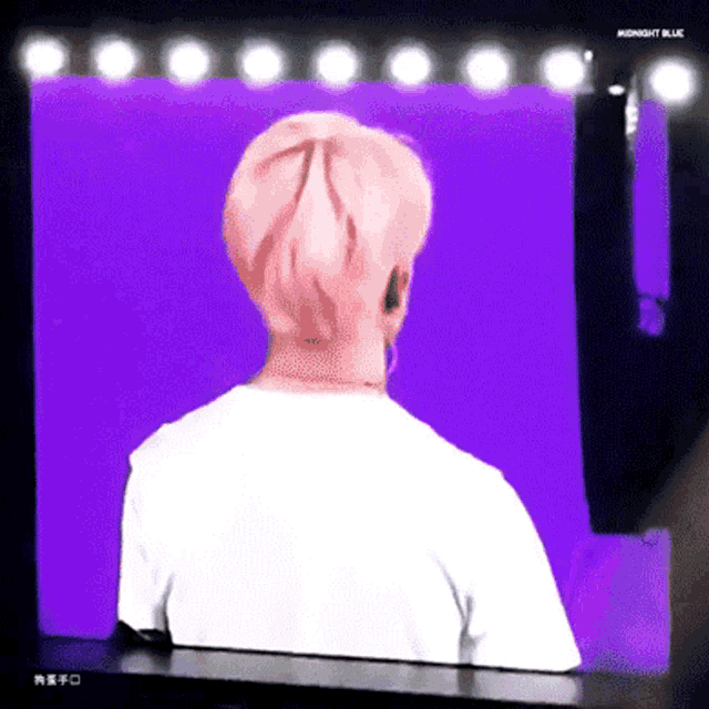 a man with pink hair is standing in front of a purple screen with the words midnight blue written on it