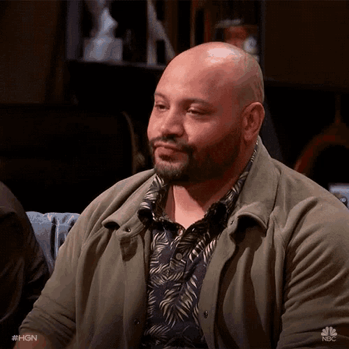 a bald man with a beard is wearing a green jacket and a shirt with palm leaves on it