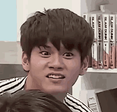 a young man in a striped shirt is making a funny face in front of a bookshelf .
