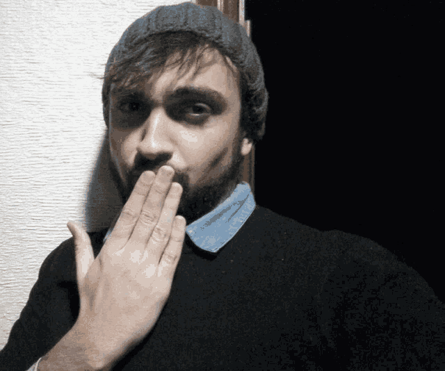 a man with a beard wearing a beanie covering his mouth