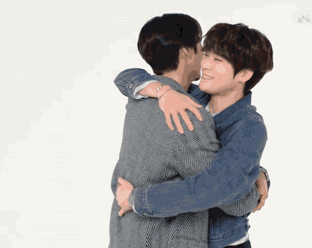 a man in a denim jacket is hugging another man
