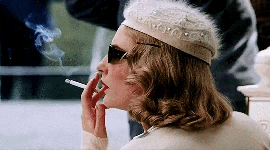 a woman smoking a cigarette wearing a white hat and sunglasses