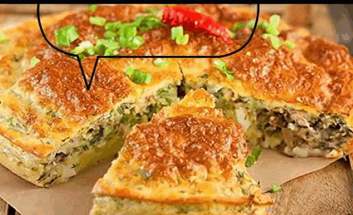 a pie with green onions and a red pepper on top is sitting on a wooden table .