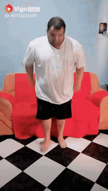 a man in a white shirt and black shorts is standing in front of a red couch covered in a red blanket