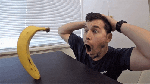 a man wearing a converse shirt is looking at a banana with his mouth open