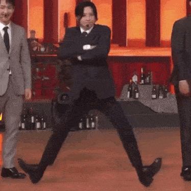 a man in a suit is dancing on a stage in front of bottles of wine .