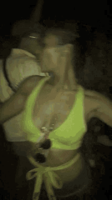 a woman in a neon yellow bikini top is dancing in a dark room