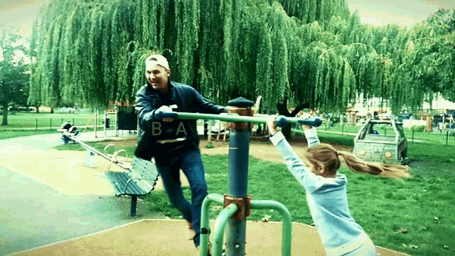 a man and a girl are playing on a playground with the letters b and a visible in the background