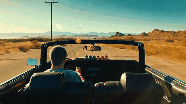 a man is driving down a desert road in a convertible car
