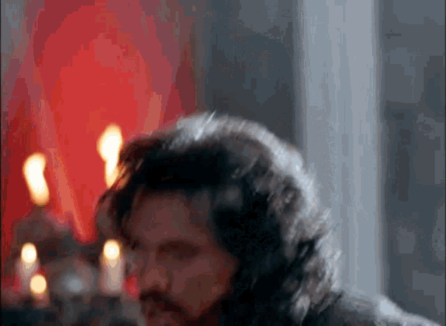 a man with long hair and a beard is standing in front of candles in a room .