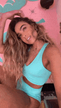 a woman is taking a selfie in front of a pink wall while wearing a blue top and shorts .