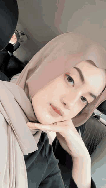 a woman in a hijab is sitting in a car with her hand on her chin