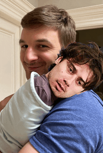 a man in a blue shirt is holding a baby wrapped in a white blanket