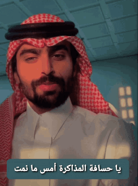 a man with a beard wearing a keffiyeh and a white shirt with arabic writing on it