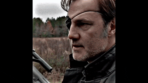 a man wearing sunglasses and a patch on his eye is standing in front of trees .