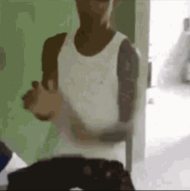 a man in a white tank top is standing in front of a door