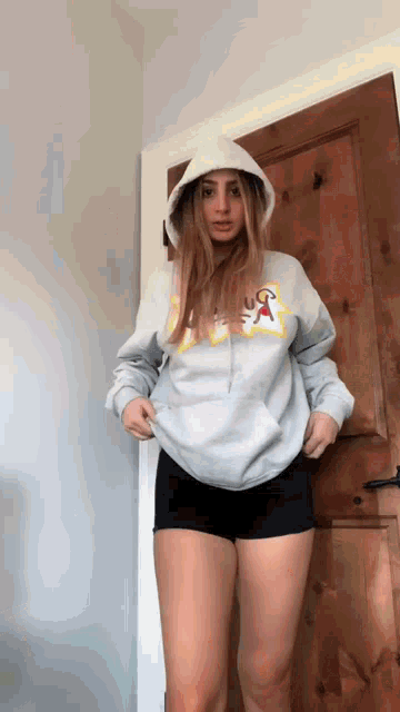 a girl wearing a hoodie and shorts is standing in front of a wooden door .