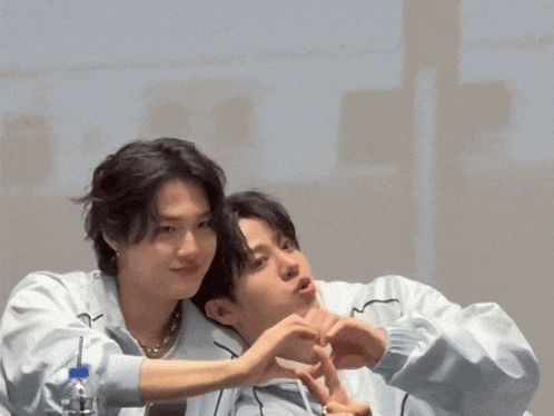 two young men are making a heart shape with their fingers