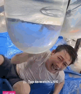 a man is laying on a blue tarp with a balloon in his mouth .