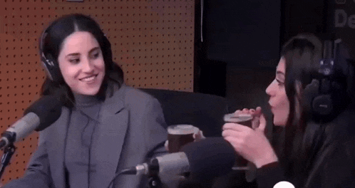 two women are sitting at a table in front of a microphone .