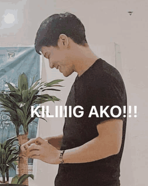 a man in a black shirt is standing in front of a plant and a sign that says " kiliiig ako !! "