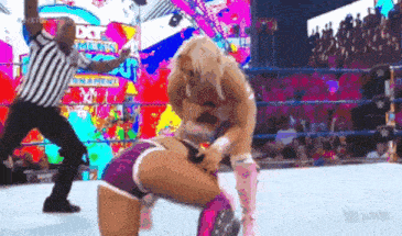 two women are wrestling in a wrestling ring with a referee watching .