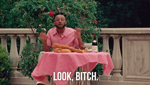 a man in a pink shirt is sitting at a table with a checkered table cloth and a bottle of wine ..