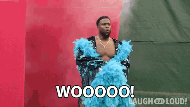 a man in a blue feather boa is standing in front of a red wall and says woooo !