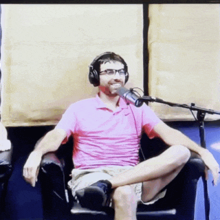 a man in a pink shirt and headphones is sitting in front of a microphone