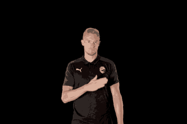 a man wearing a black puma shirt holds his hand to his heart