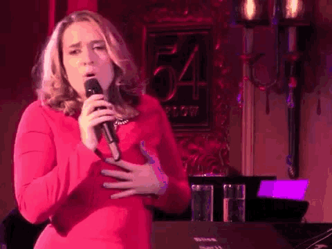 a woman in a red dress is singing into a microphone in front of a sign that says 54 row .