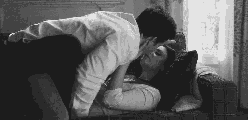 a black and white photo of a man kissing a woman on a couch .