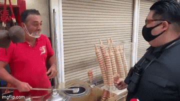 a man wearing a face mask is talking to another man who is selling ice cream .