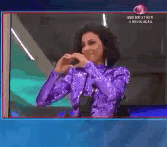 a woman in a purple dress is making a heart shape with her hands on a screen .