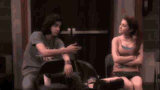 a man and a woman are sitting in chairs and the man is pointing at the woman