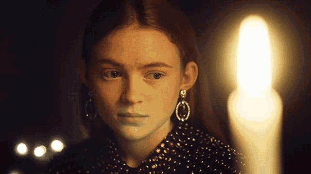 a close up of a girl with a candle in the background