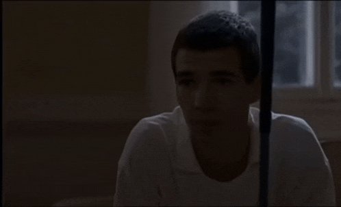 a man in a white shirt sits in a dark room
