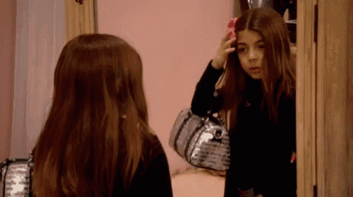 a girl is looking at herself in a mirror .